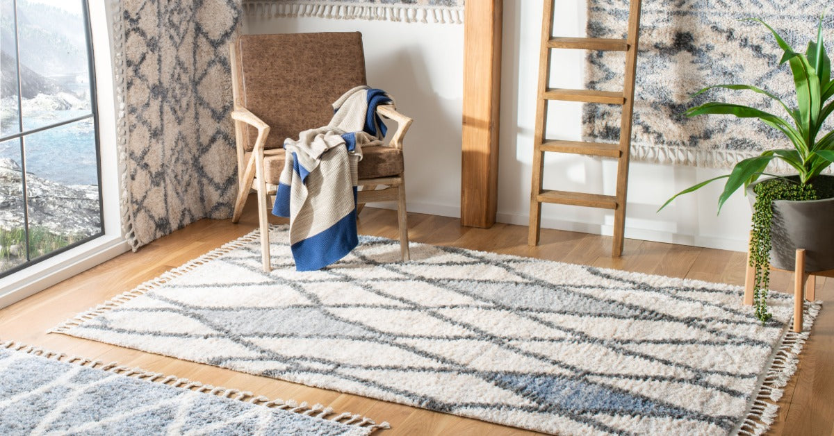 A bright room with patterned rugs, a wooden chair, a draped blanket, a ladder, a plant, and large windows.